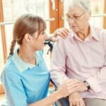 Caregiver and senior woman in nursing home talking and touching